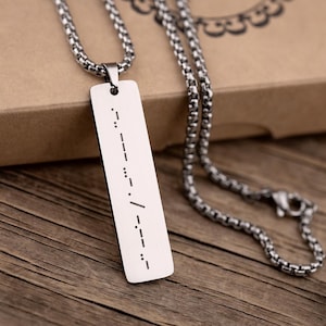 May include: A silver chain necklace with a rectangular pendant. The pendant has a message written in braille.