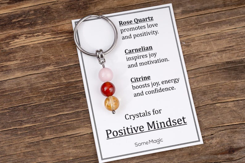 May include: A keychain with a silver ring and three gemstone beads: rose quartz, carnelian, and citrine. The accompanying card reads "Crystals for Positive Mindset" and lists the properties of each crystal.