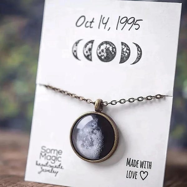 Peut inclure: Un collier avec un pendentif rond représentant une phase lunaire. Le pendentif est serti dans un cadre de couleur bronze et est suspendu à une chaîne délicate. La carte indique "Oct 14, 1995" et "Made with Love".