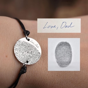 Puede incluir: Una pulsera de plata con un dije redondo que presenta una huella digital y la inscripción "Love, Dad".