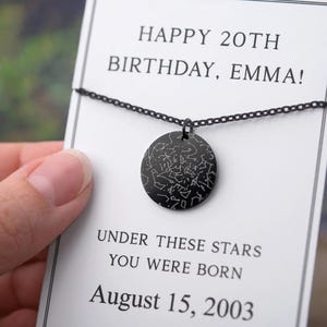 Può includere: Una collana con pendente nero con un ciondolo circolare con un design a mappa stellare. La collana è esposta su una carta bianca con il testo "HAPPY 20TH BIRTHDAY, EMMA!" e "UNDER THESE STARS YOU WERE BORN August 15, 2003".