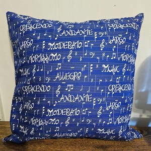 May include: Blue throw pillow with a white musical note pattern. The pillow features musical terms like "crescendo", "andante", "largo", and "allegro".