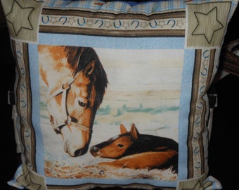 May include: A blue and brown pillow with a picture of a horse and foal. The pillow has a border of brown horseshoes and stars.
