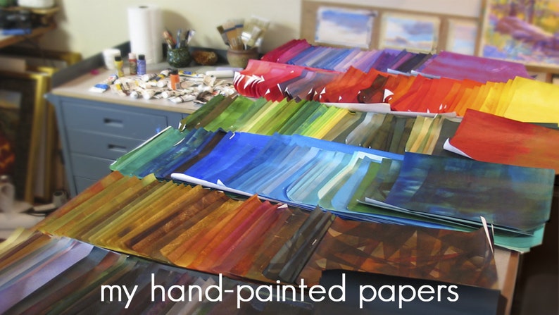 May include: A table covered in stacks of hand-painted papers in various colours, including red, orange, yellow, green, blue, and purple. The text "my hand-painted papers" is visible at the bottom of the image.