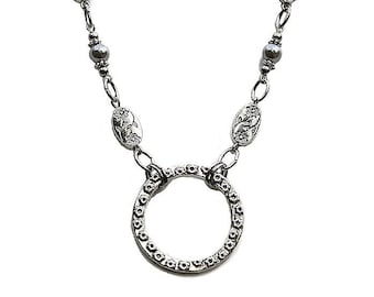 May include: A silver necklace with a floral design and a circle pendant. The necklace has small gray beads and oval charms with floral details.