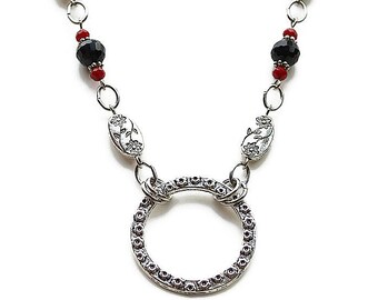 May include: A silver necklace with a large circle pendant, black and red beads, and floral accents.