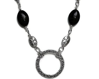 May include: Silver-toned necklace featuring a large, ornate circular pendant and oval floral accents. The necklace incorporates black oval beads. The design is symmetrical, with the pendant at the center and the beads and floral accents on either side.