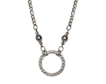May include: A silver chain necklace with two dark gray beads and a silver circle pendant with a textured design.