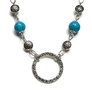 Può includere: Una collana d'argento con perline turchesi e un ciondolo circolare d'argento. La collana è realizzata in metallo e ha un design semplice.