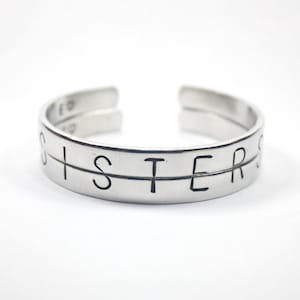 May include: A silver bracelet with the word "Sister" engraved on it.