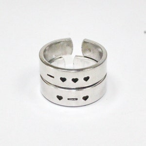 Puede incluir: Dos anillos de plata con un diseño de corazón. Los anillos son abiertos y se pueden ajustar para que quepan en diferentes tamaños de dedos.