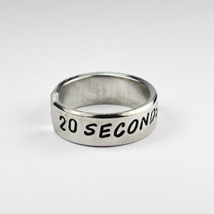 Könnte beinhalten: Ein silberner Ring mit der Gravur "20 SECONDS".