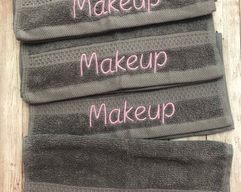 May include: Four gray towels with the word "Makeup" embroidered in pink on each towel.