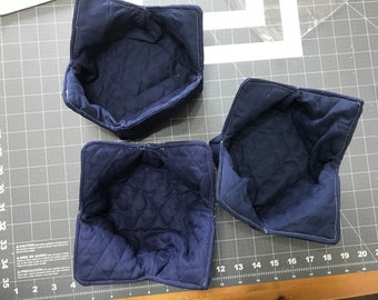May include: Three blue quilted fabric bowls, folded and ready to use. The bowls are made of a soft, quilted fabric and have a square shape.