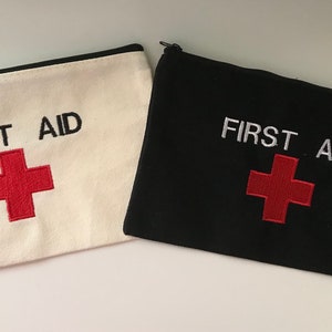May include: Two zippered pouches, one white and one black, with the words "FIRST AID" and a red cross embroidered on each.