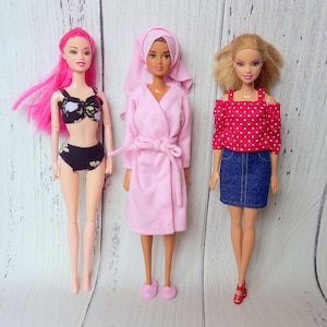 May include: Three fashion dolls in various outfits. One doll wears a black bikini with a floral pattern and pink hair. Another doll is in a pink robe and towel. The third doll is in a red polka dot top and denim skirt.