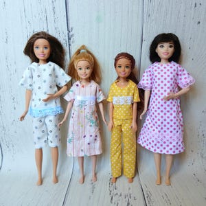 May include: Four dolls standing in a row. The first wears a white top and pants with black star patterns and blue trim. The second wears a pink striped dress with floral prints. The third wears a yellow polka dot top and pants. The fourth wears a pink polka dot dress.