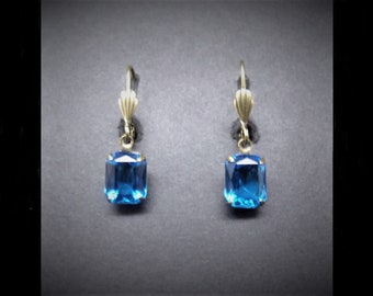 May include: A pair of gold dangle earrings with a square blue gemstone.