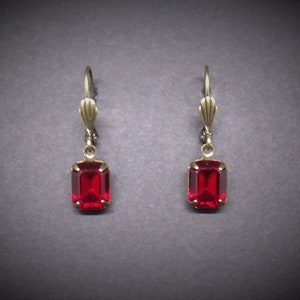 May include: A pair of dangle earrings with red gemstone accents and gold-toned metal.