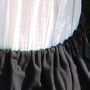 May include: A white, sheer fabric top with a black, gathered fabric skirt. The skirt has a ruffled edge.