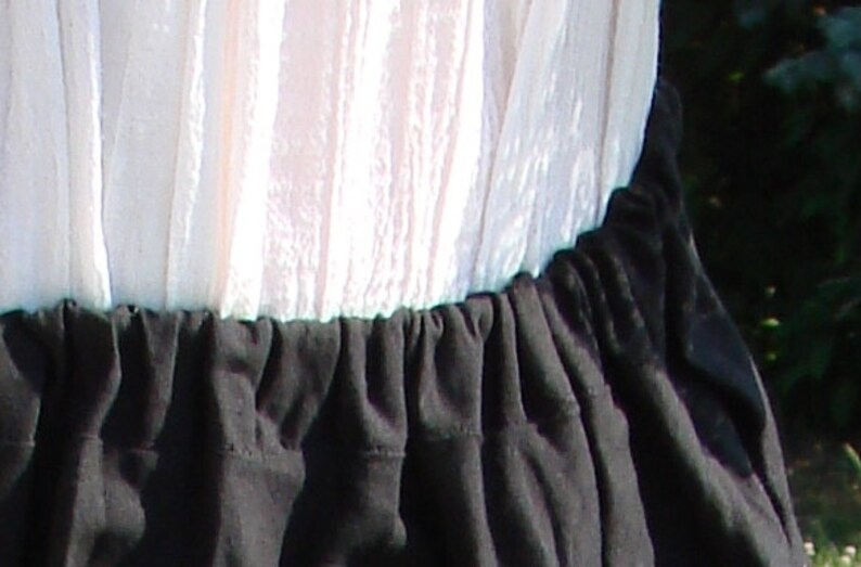 May include: A white, sheer fabric top with a black, gathered fabric skirt. The skirt has a ruffled edge.
