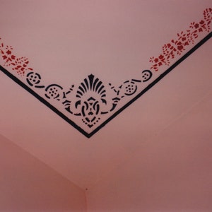 May include: A pink ceiling with a black and red stencil design. The design features a floral pattern with a central ornate motif.