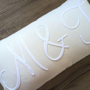 May include: White pillow with the letters "M & J" embroidered in a cursive font.