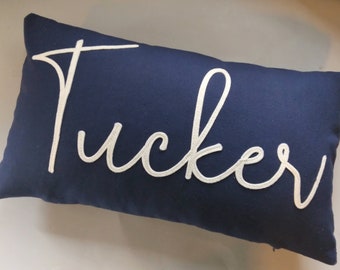 May include: A navy blue pillow with the name "Tucker" embroidered in white.
