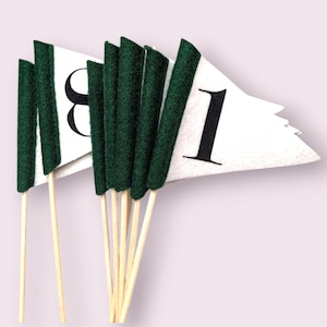May include: A set of white pennant flags with black numbers, each attached to a wooden stick. The flags have a dark green felt trim. The numbers are 8 and 1. The flags are arranged in a fan shape.