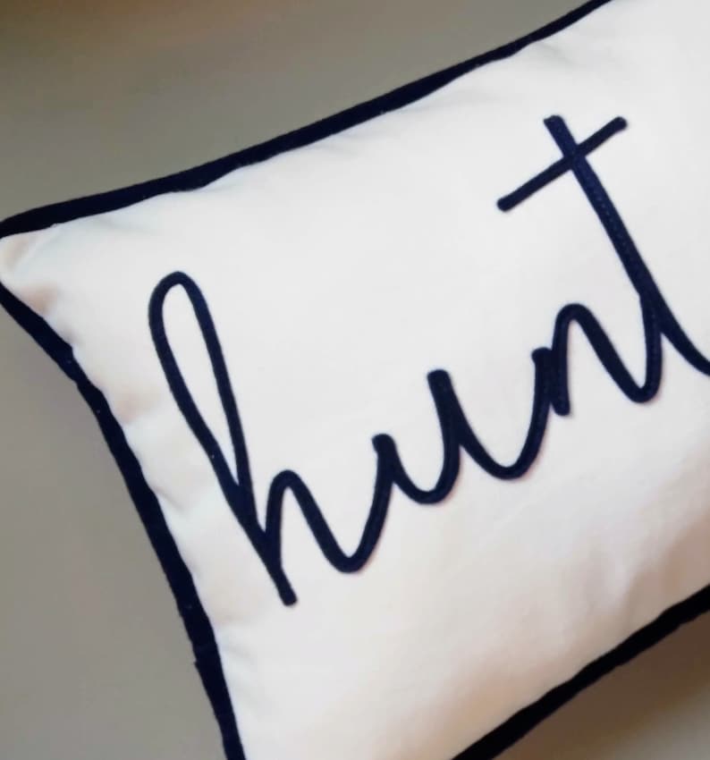 Puede incluir: Almohada blanca con borde azul marino y la palabra "hunt" bordada en cursiva azul marino.