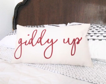 May include: A white pillow with the words "giddy up" written in red cursive script.