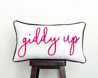May include: White pillow with black trim and the words "giddy up" written in pink cursive.