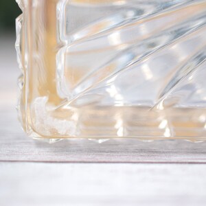 K&ouml;nnte beinhalten: Nahaufnahme eines transparenten Glasobjekts mit einem geometrischen, f&auml;cherartigen Muster. Das Objekt hat eine rechteckige Form mit einer strukturierten Oberfl&auml;che. Das Glas hat einen leichten Bernsteinton.