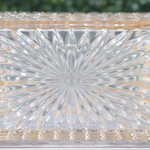 K&ouml;nnte beinhalten: Transparente, rechteckige Glasbox mit einem Sonnenstrahlenmuster auf der Oberseite. Die Box hat einen dekorativen, strukturierten Rand. Das Glas ist transparent. Wahrscheinlich zur Aufbewahrung oder Pr&auml;sentation.
