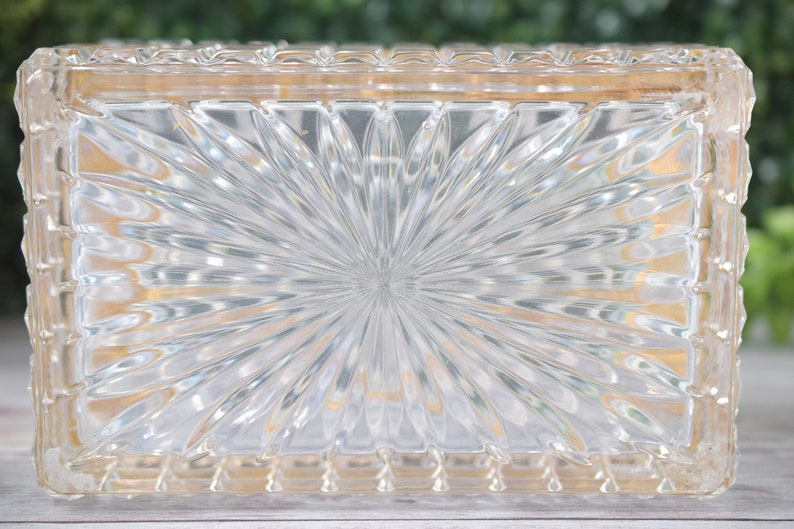 K&ouml;nnte beinhalten: Transparente, rechteckige Glasbox mit einem Sonnenstrahlenmuster auf der Oberseite. Die Box hat einen dekorativen, strukturierten Rand. Das Glas ist transparent. Wahrscheinlich zur Aufbewahrung oder Pr&auml;sentation.
