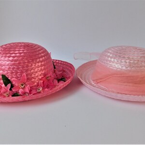 May include: Two pink straw hats with a wide brim. One hat has a pink flower trim and the other has a pink ribbon.