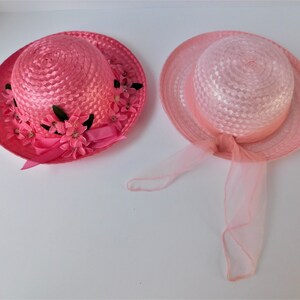 May include: Two pink straw hats with floral embellishments. One hat has a pink ribbon and the other has a pink tulle bow.