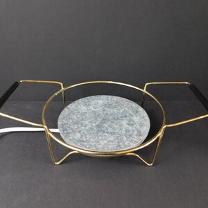 May include: A vintage gold-toned metal warming tray with a round, speckled gray stone surface. The tray has black handles and a white power cord. A classic piece for serving warm dishes.