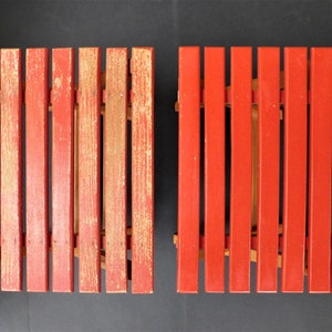 May include: Two red wooden folding chairs with a slatted design. The chairs are made of wood and have a red paint finish. The chairs are in good condition and have a vintage look.