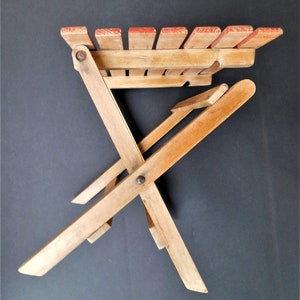 May include: A wooden folding chair with a red painted top. The chair is made of natural wood and has a simple design.