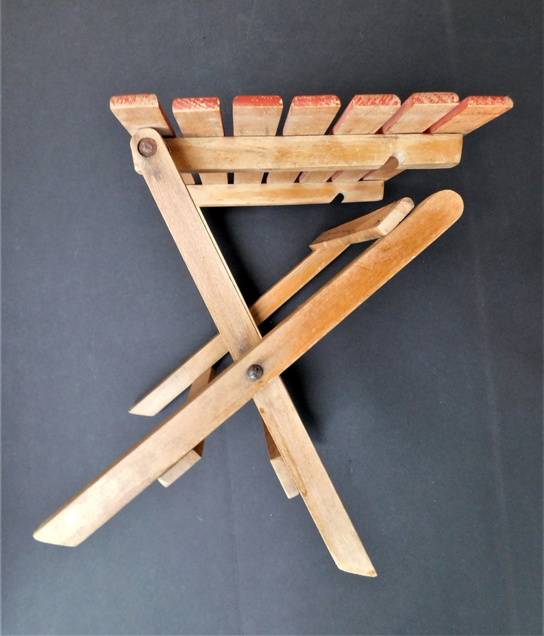 May include: A wooden folding chair with a red painted top. The chair is made of natural wood and has a simple design.