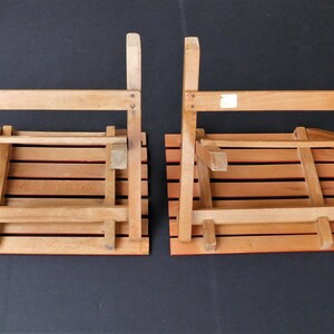 May include: Two wooden folding chairs with slatted seats and backs. The chairs are folded and are sitting on a black surface.