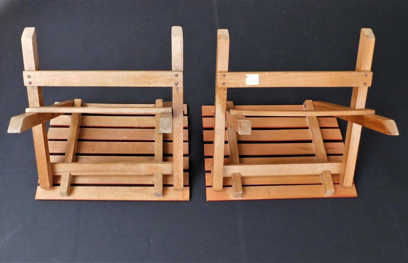 May include: Two wooden folding chairs with slatted seats and backs. The chairs are folded and are sitting on a black surface.
