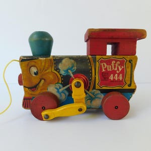 May include: Vintage wooden pull toy train with a smiling face and the word "Puffy 444". The train is painted in yellow, red, and blue with a yellow pull string. A classic toy.