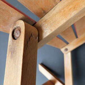 May include: Close-up of a wooden chair with a red stripe on the seat. The chair is made of light brown wood and has a simple design. The chair is in good condition, but shows signs of wear and tear.