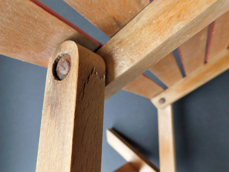 May include: Close-up of a wooden chair with a red stripe on the seat. The chair is made of light brown wood and has a simple design. The chair is in good condition, but shows signs of wear and tear.