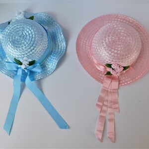 May include: Two straw hats with ribbon ties and flower embellishments. One hat is light blue and the other is pink.