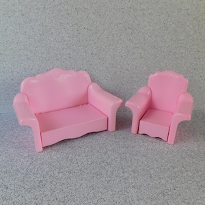 May include: A pink plastic dollhouse sofa and armchair set. The sofa has a curved back and arms, while the armchair has a straight back and arms.