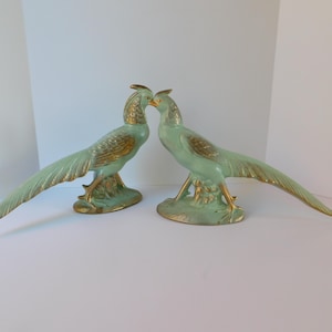 May include: A pair of ceramic pheasant figurines in a light green glaze with gold accents. The birds are facing each other with their heads tilted down.