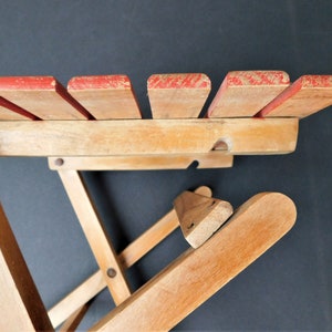 May include: A wooden folding chair with red painted slats on the back. The chair is made of natural wood and has a simple design.